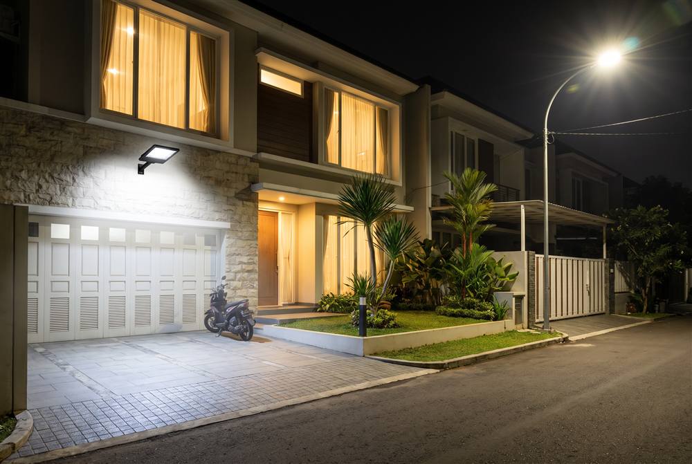 Floodlight menerangi halaman rumah dan lampu jalan menyala di depan pada malam hari