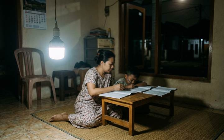 Ibu dan anak belajar saat mati listrik, diterangi satu bohlam